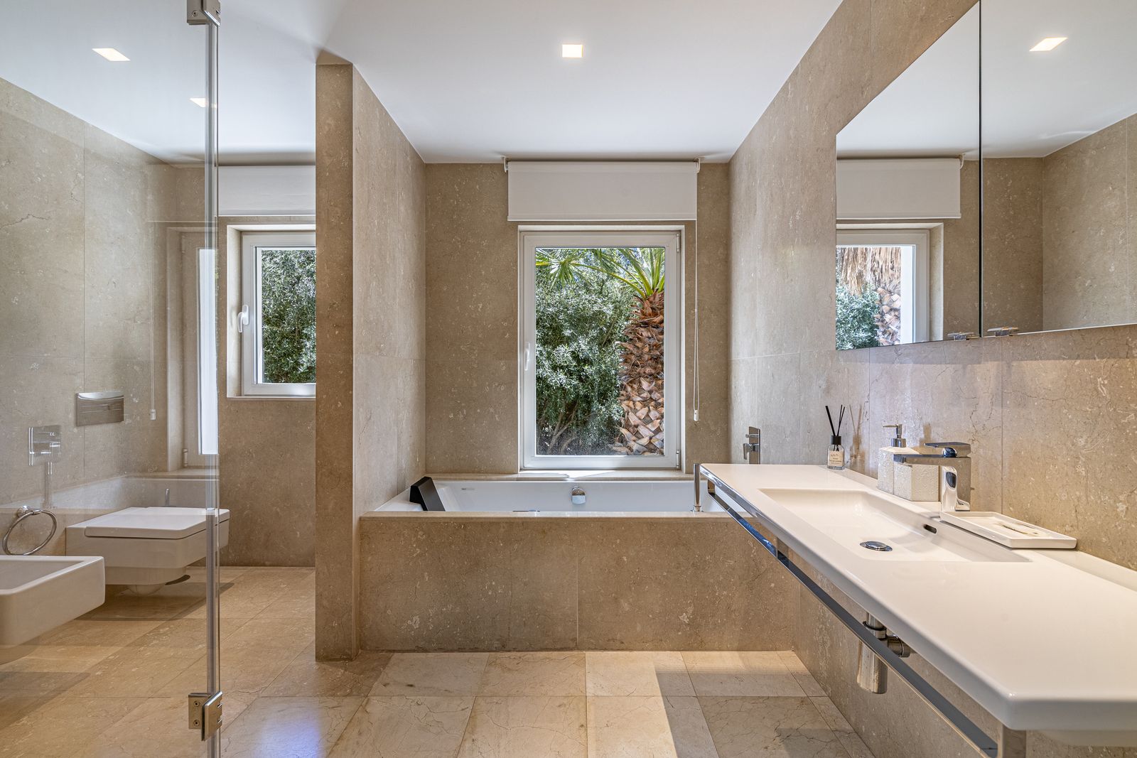 Beige stone bathroom with a built-in bath, long vanity unit and glass-enclosed shower