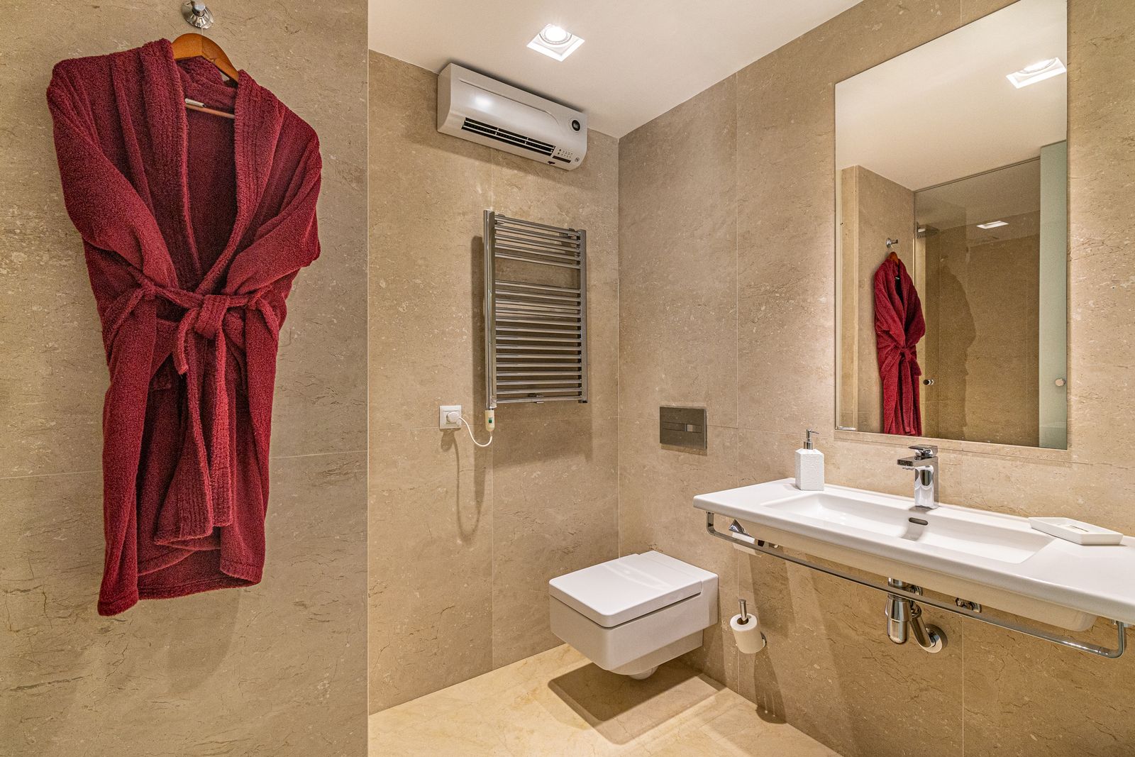 Beige bathroom with a red bathrobe, a mirror, a vanity basin and a heated towel rail