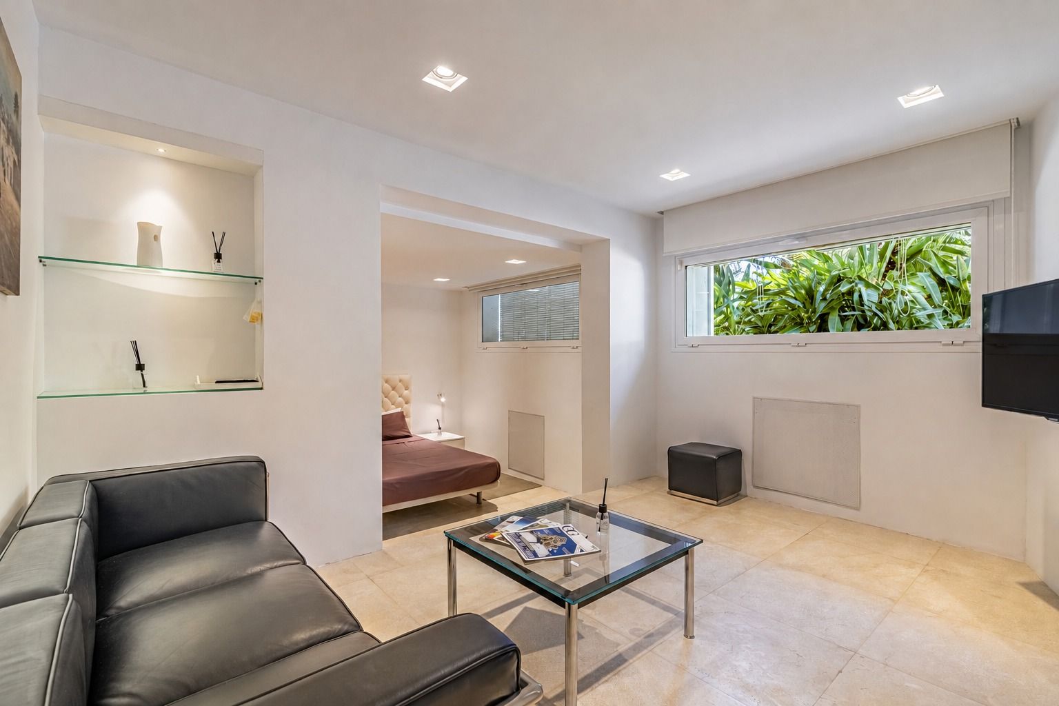 Suite sitting area with a dark sofa, glass coffee table and a window overlooking greenery