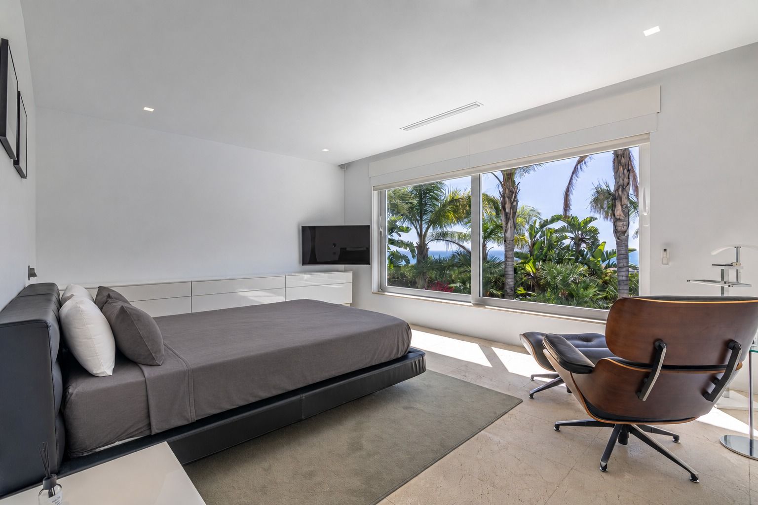 Bedroom with a large window onto the palm garden and a brown leather armchair