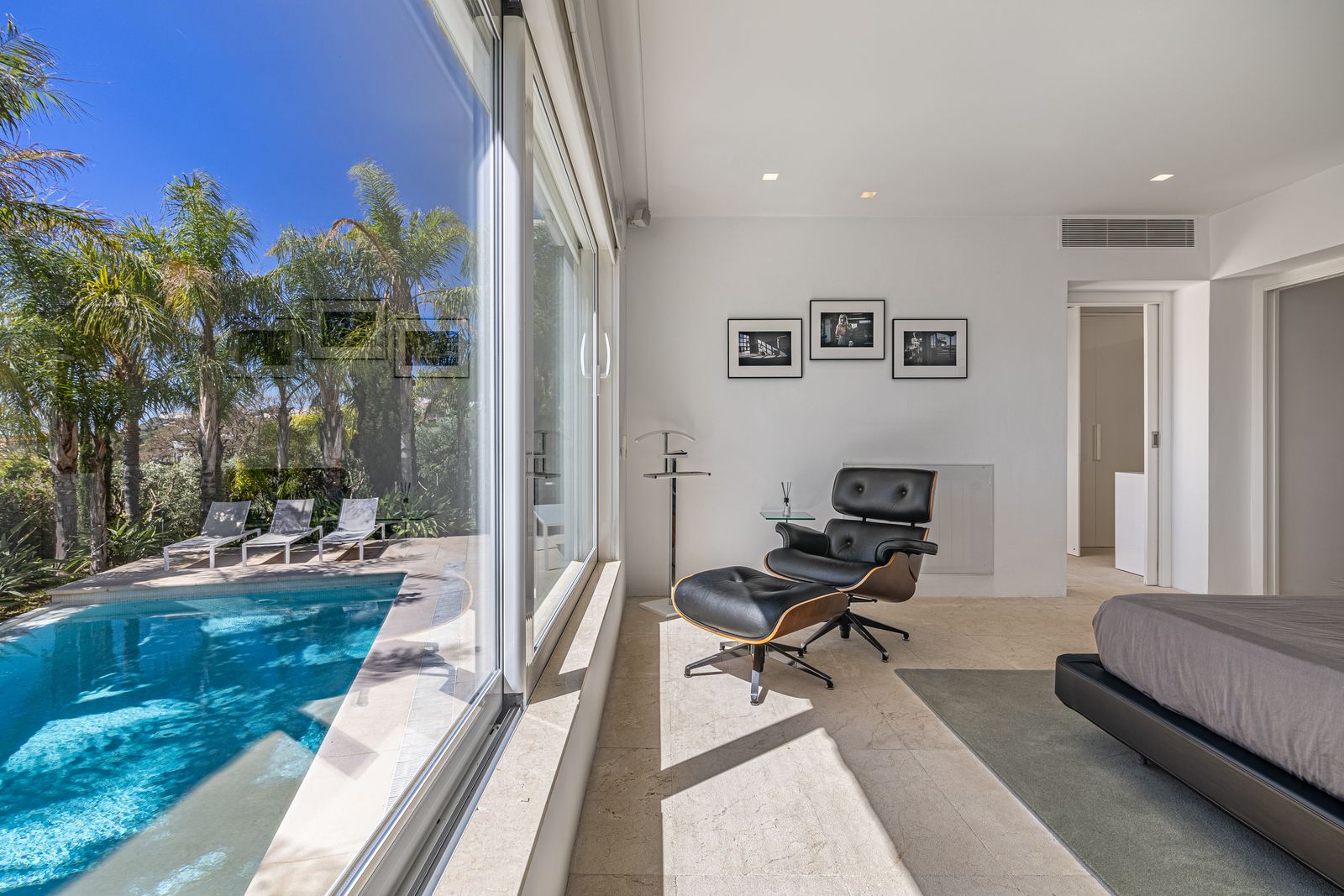 Bedroom with floor-to-ceiling glass doors overlooking the pool and an armchair with a footstool