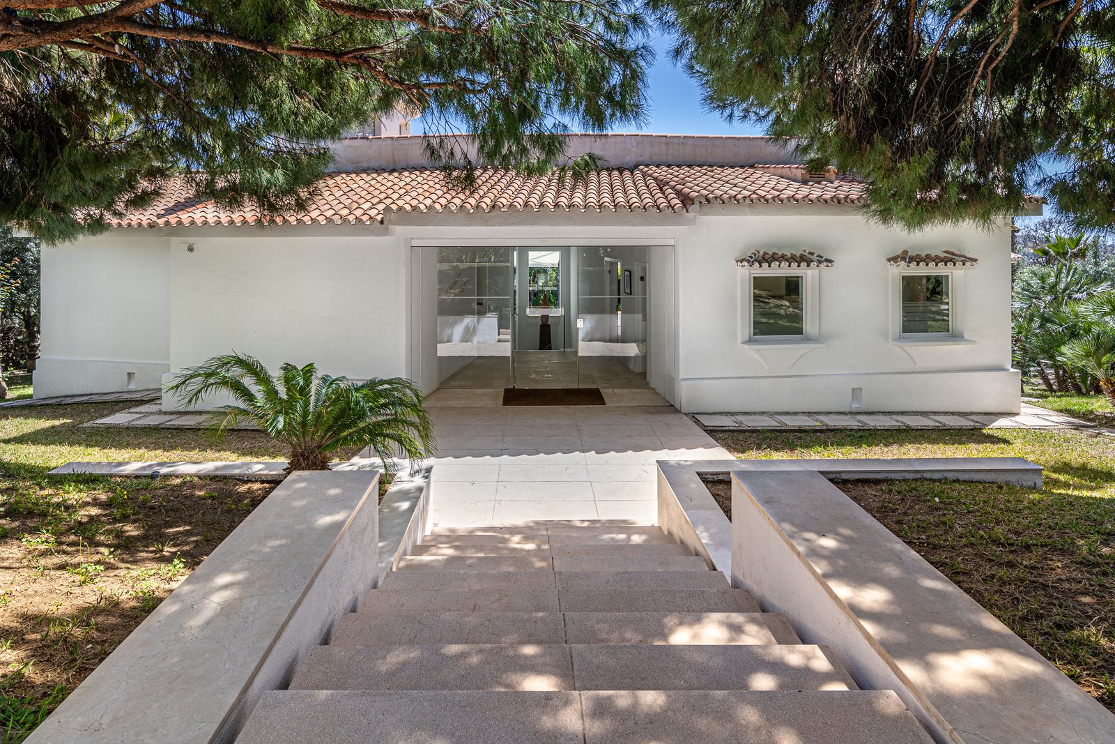 Stone steps leading to the white façade of Villa Coníferas beneath the trees