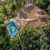 Aerial view of the villa's terracotta roofs and pool among the palm trees