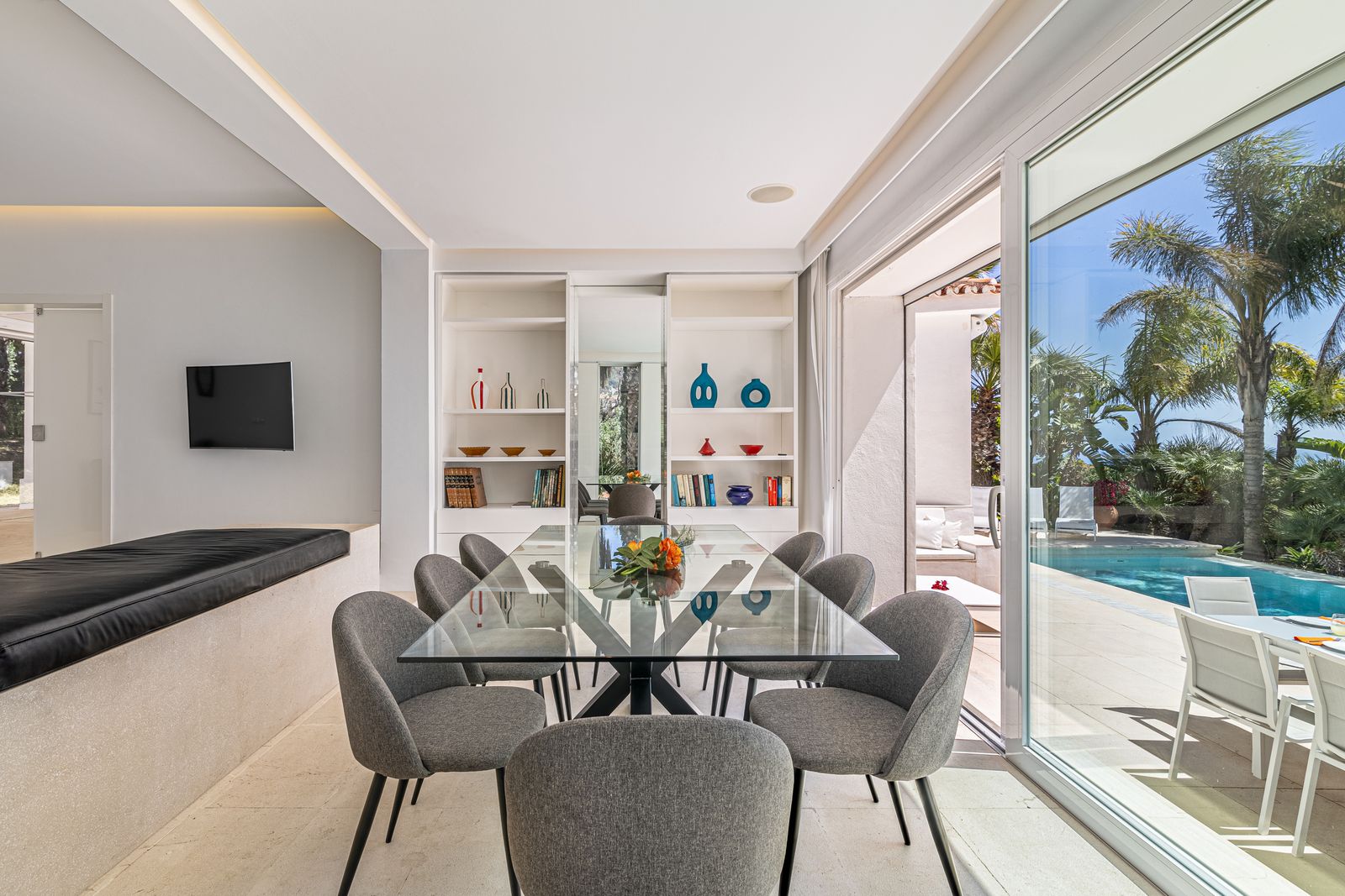 Indoor dining area with a glass table, chairs and glass doors overlooking the pool terrace