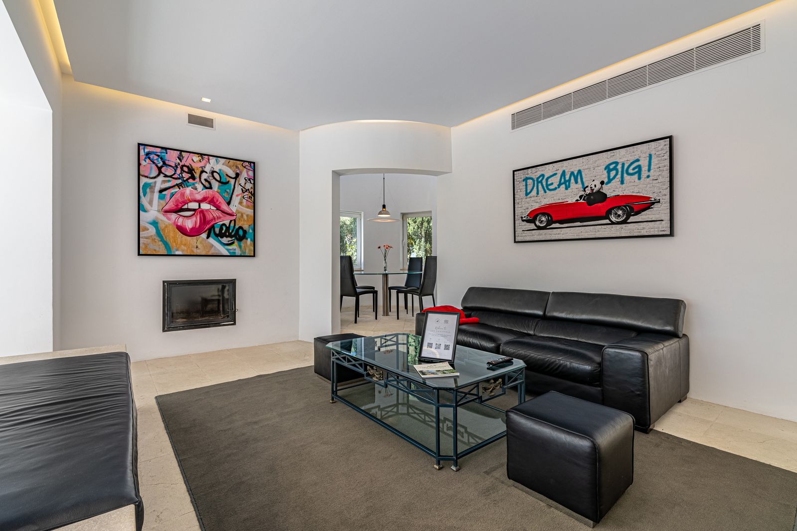 Living room with a fireplace, a black leather sofa and colourful pop-art pictures