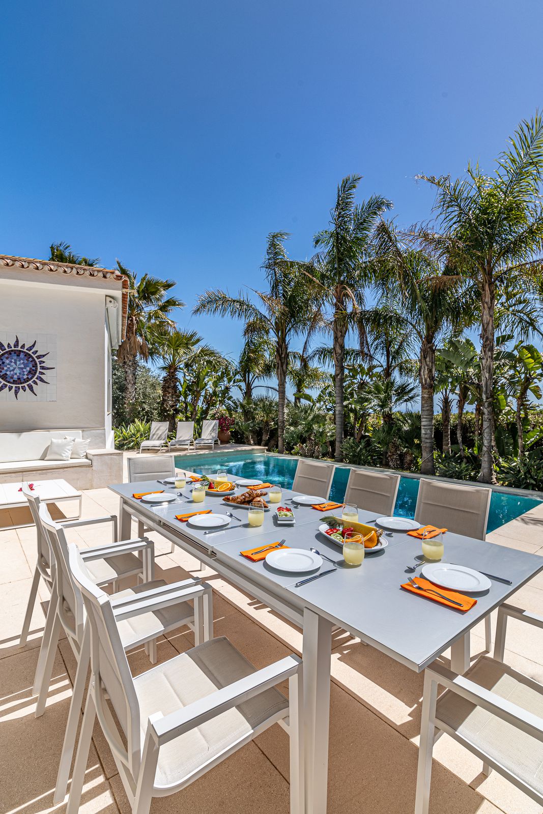 Long outdoor dining table set with plates and napkins beside the pool